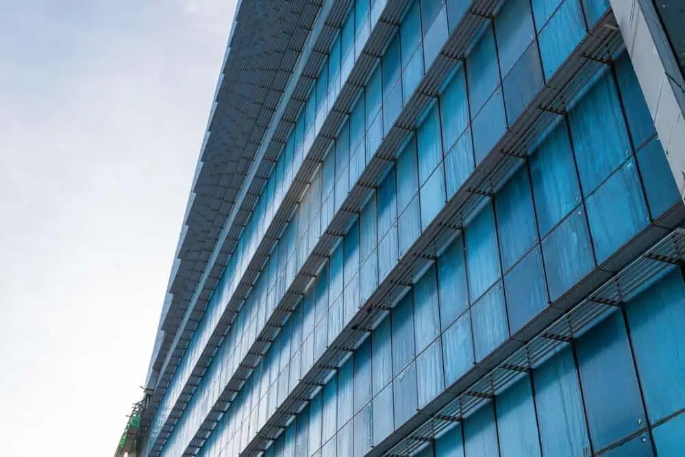 Close-up of a modern commercial building facade with blue-tinted glass panels and sleek horizontal lines, viewed from a low angle, showcasing its pristine exterior renovation.