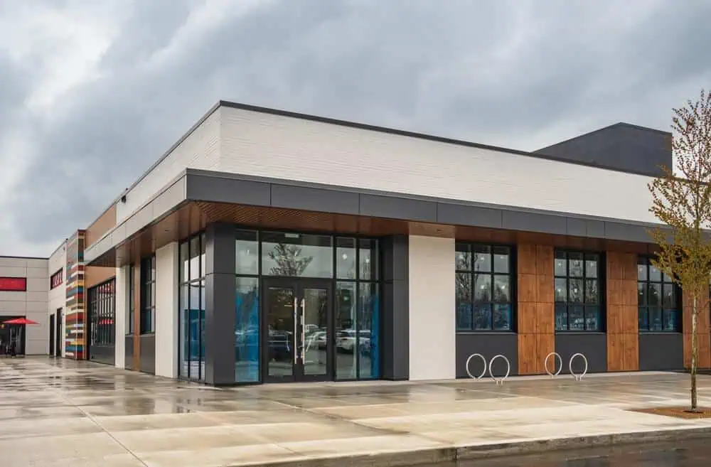 Modern commercial building with large windows, wood and white paneling, showcasing expert roofing services in Bethesda; rainy pavement enhances contemporary design.