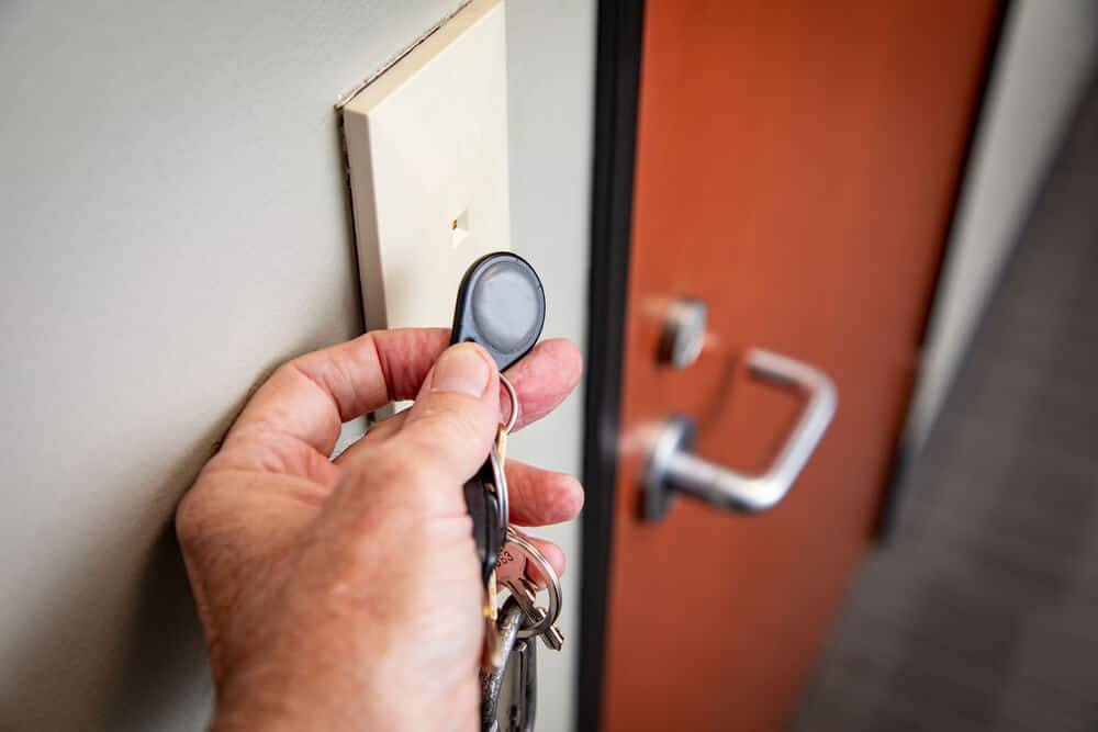 Close-up of a hand holding keys with a key fob, poised to tap a card reader near a modern door handle in a freshly renovated space.