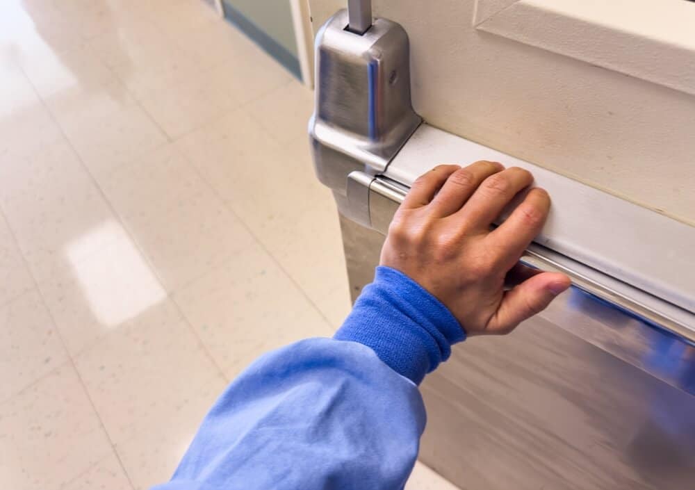 Image of a person in medical scrubs opening a modern metal door in a hospital hallway, highlighting top-quality renovation and construction services for healthcare facilities.