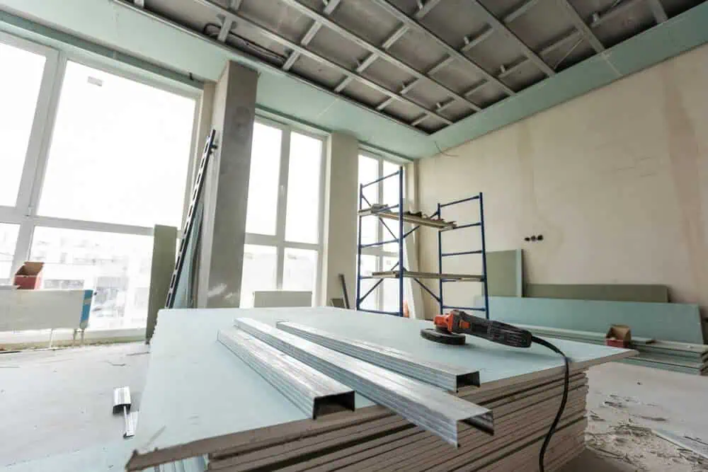 Construction site featuring large windows, drywall sheets, metal studs, power tool, and scaffold for exterior and interior renovation services.