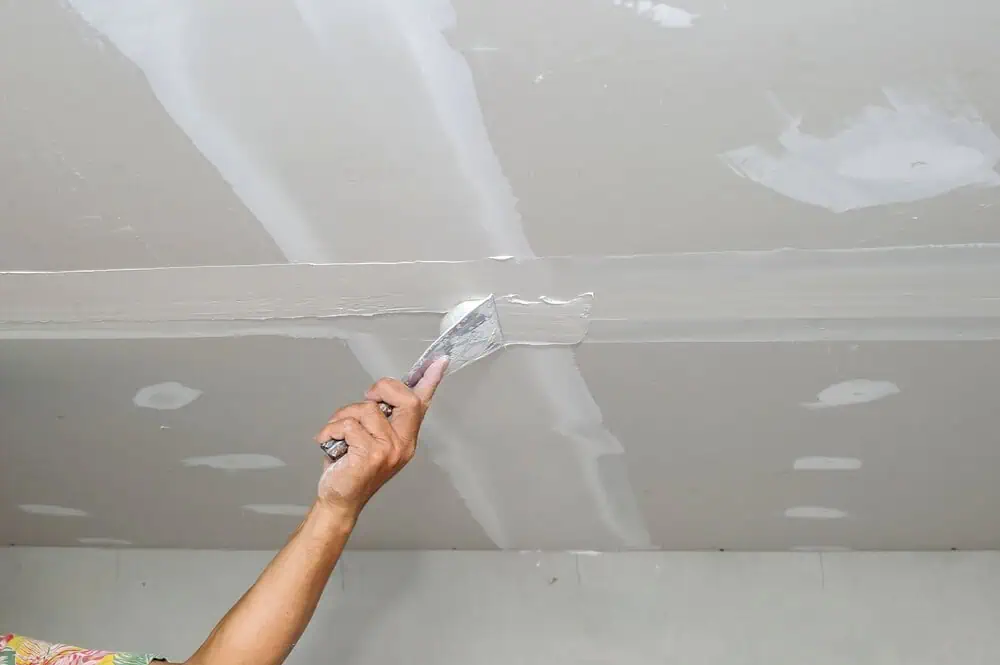 Skilled worker using trowel to apply plaster on ceiling seam, enhancing commercial drywall project.