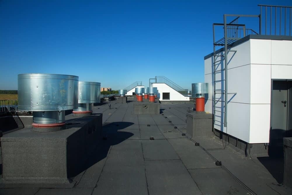 Alt text: Commercial flat roofing with ventilation units, smooth surface, access structures beneath clear blue sky - exterior renovation.