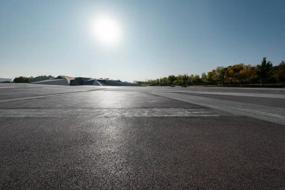 Concrete parking lot under a clear blue sky with a modern building; ideal for commercial renovation services in Arlington. Trees along the horizon enhance scenic view.