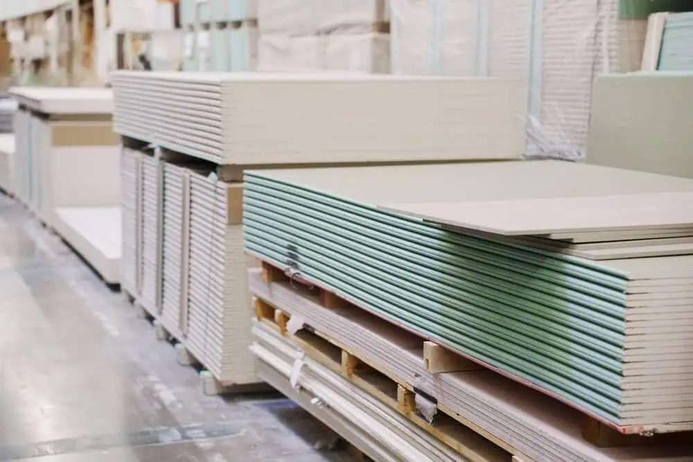 Neatly stacked commercial drywall sheets in warehouse, ready for exterior and interior renovation distribution.