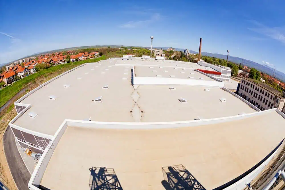 Industrial building rooftop with commercial flat roofing; surrounding landscape and urban architecture under clear blue sky. Exterior renovation and construction services.