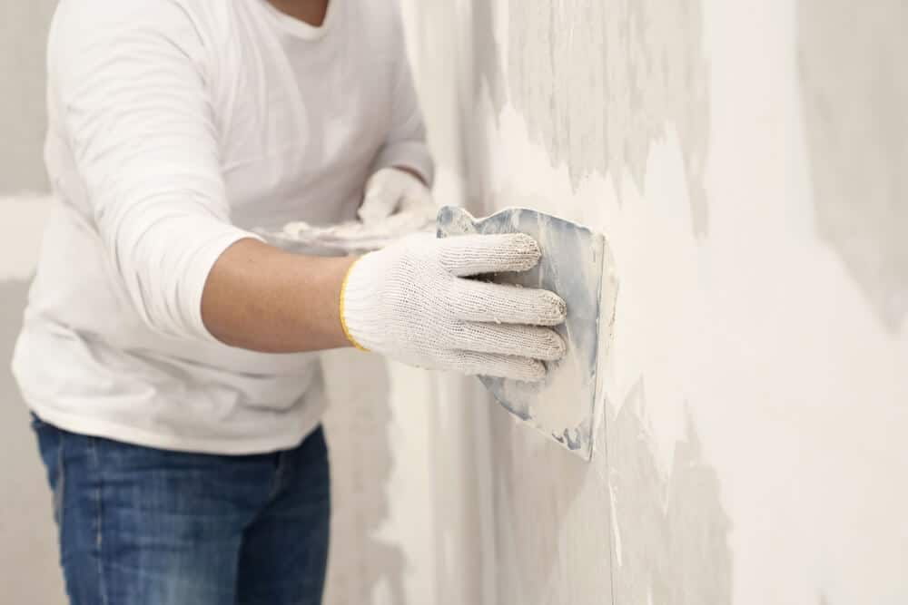 A skilled worker in white shirt and gloves applies plaster with a trowel to wall, demonstrating expert craftsmanship of Bethesda MD commercial renovation services.