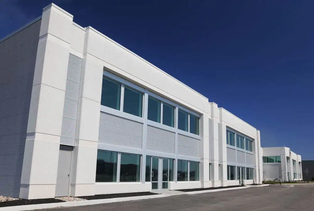 Modern white office building with large windows, sleek commercial siding, clear blue sky background; exterior renovation showcasing contemporary design.