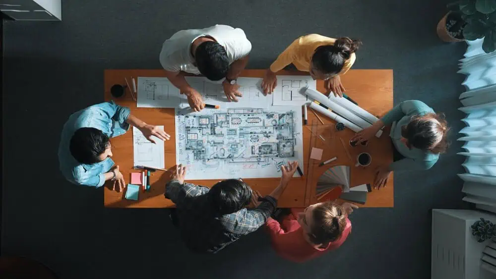 Hotel renovation contractors review architectural blueprints at a table, discussing construction plans.