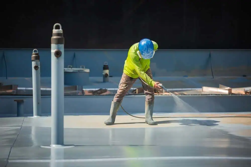 A man sprays a roof coating on top of a commercial roof.