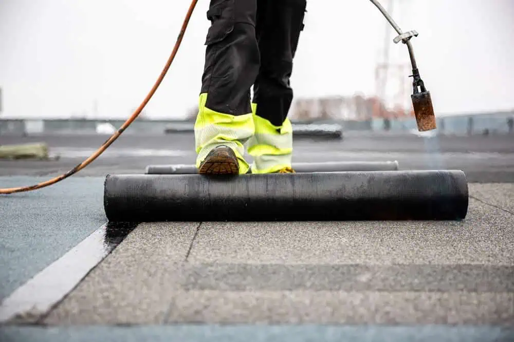 A roofer using a torch to apply a replacement roof
