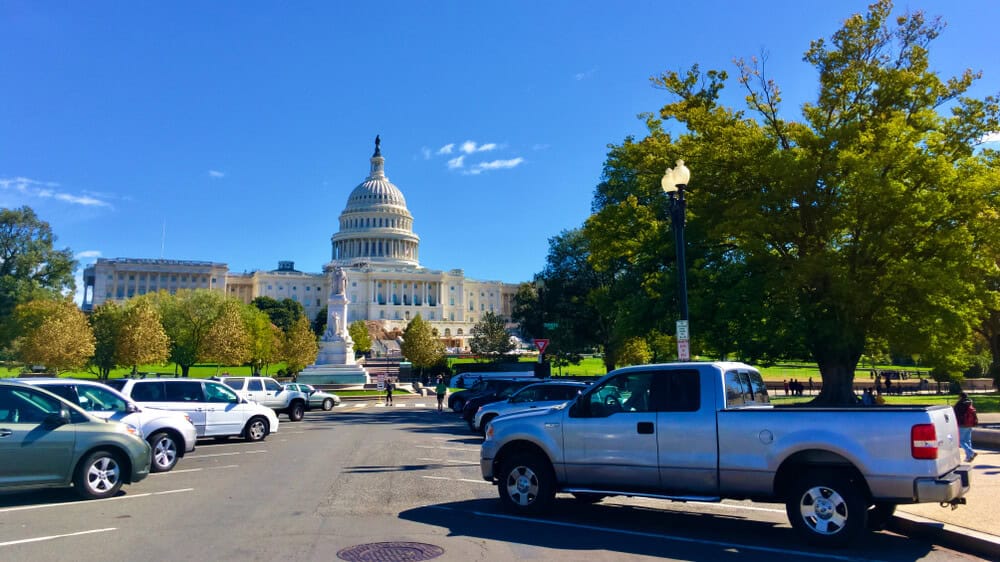 Several cars parked in front of the U.S. Capitol building, highlighting the elegant architecture under a clear blue sky; perfect inspiration for exterior renovation and construction projects.