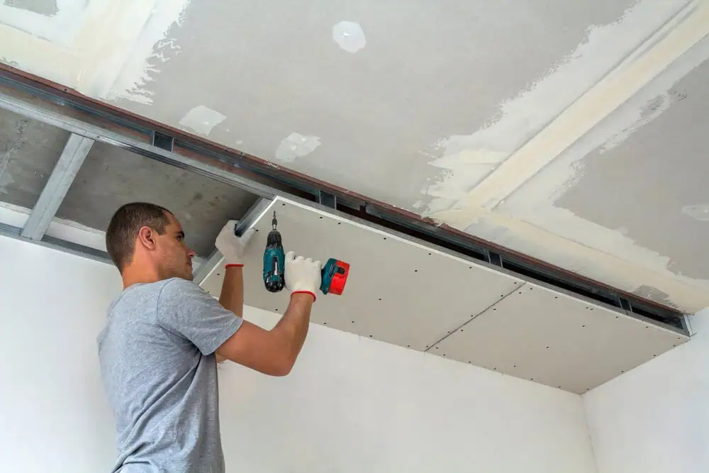 Man installs drywall on a tray ceiling