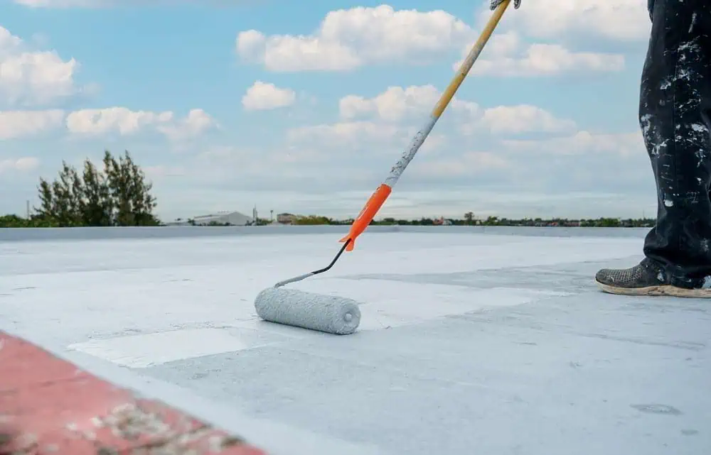 A roofing technician rolls a restoration coating onto a roof