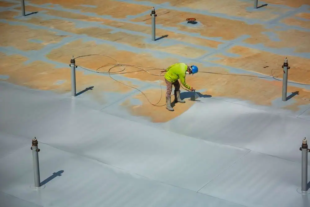 A roofer applies a spray coating during a commercial roof renovation