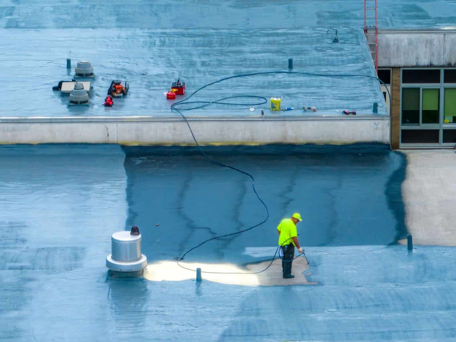 A roofer applies a spray-on coating to a commercial roof