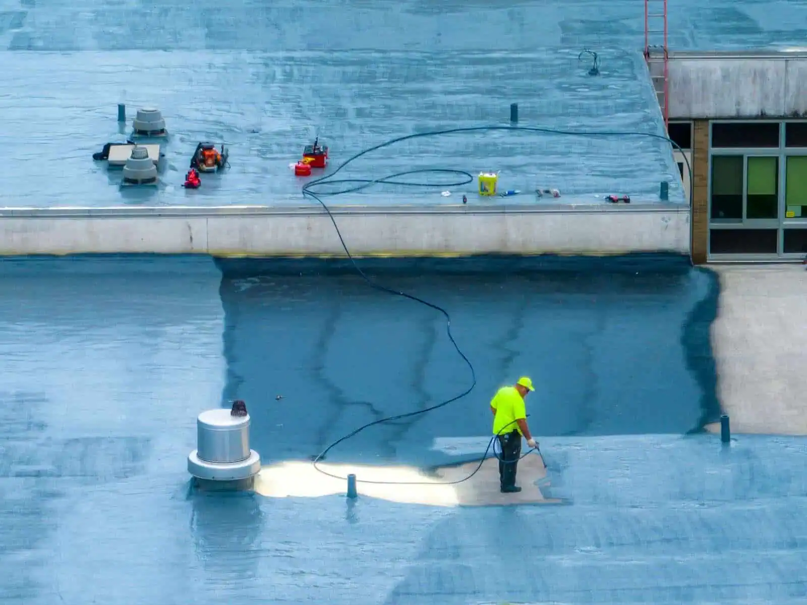 A roofer applies a spray-on coating to a commercial roof