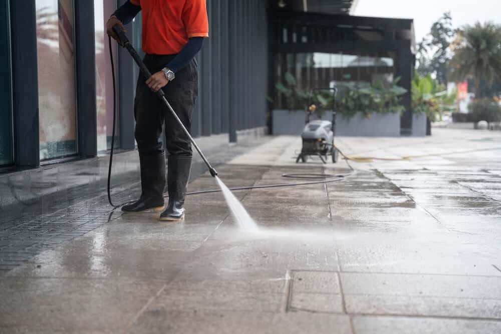 A commercial exterior cleaning service technician power washing a sidewalk