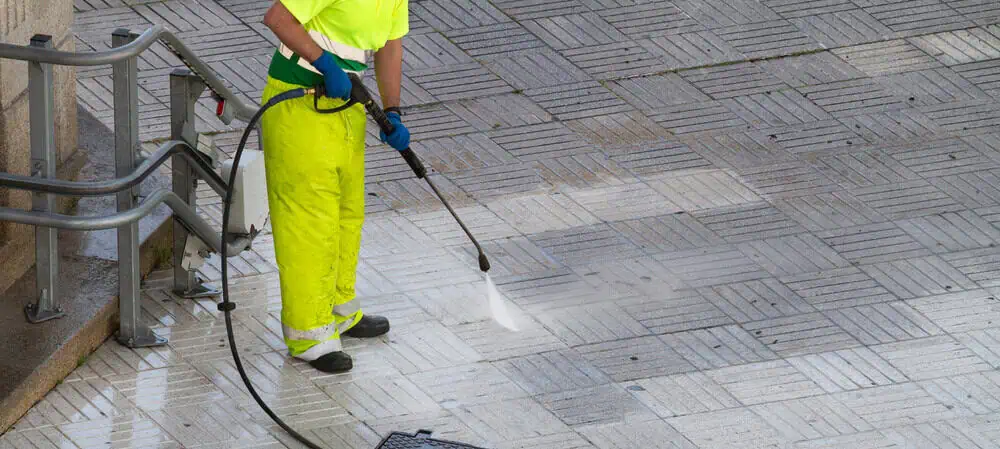 Exterior cleaning technician pressure washes commercial walkway