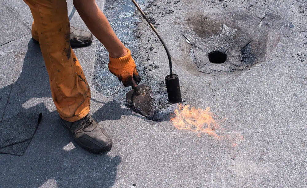A roofing technician repairs the roof around a drain