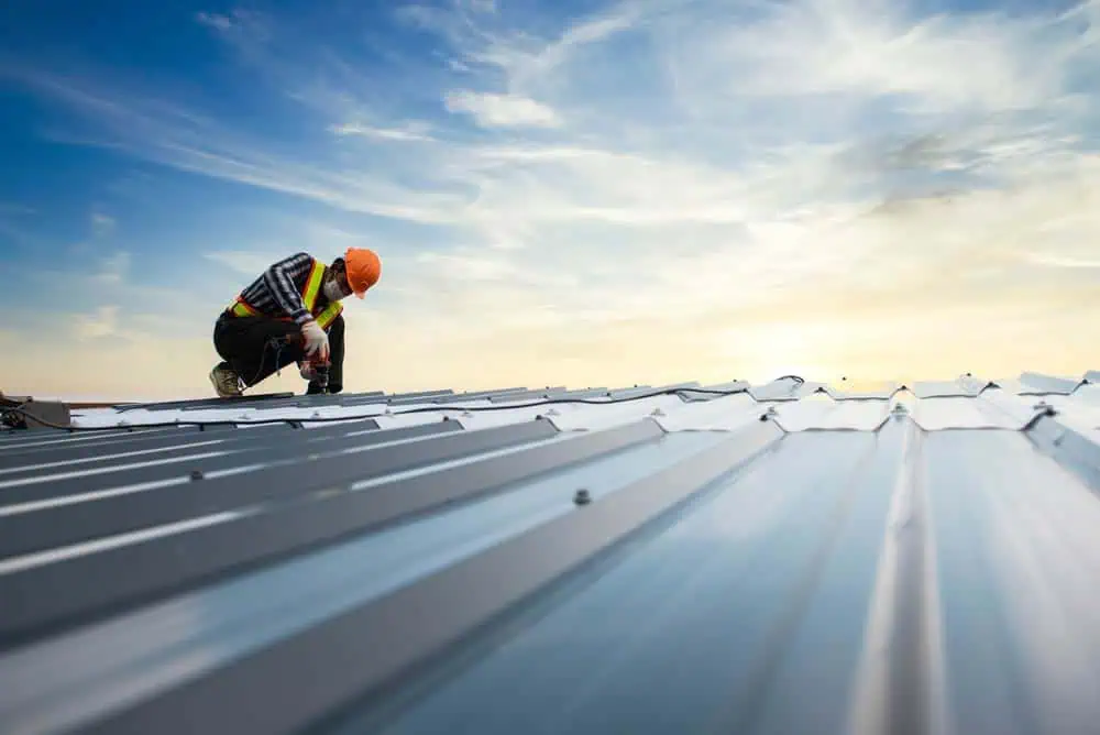 Construction worker in safety vest and helmet inspecting commercial metal roofing at sunset under partly cloudy sky, building exterior renovation and repair.